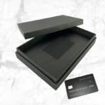 premium black card holder box matte finish with open lid showing credit card slot and black credit card on marble background