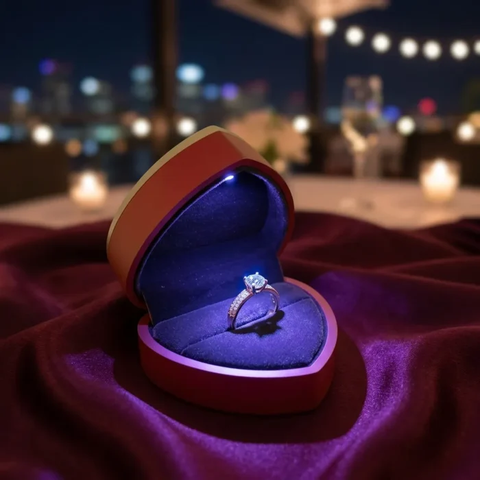Premium red heart-shaped ring box with integrated LED spotlight illuminating an engagement ring on a velvet fabric background